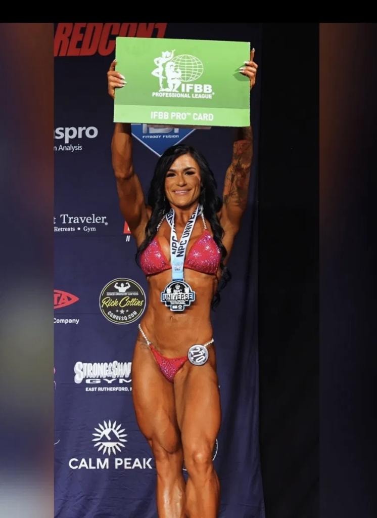 Michaela on stage holding her IFBB Pro Card